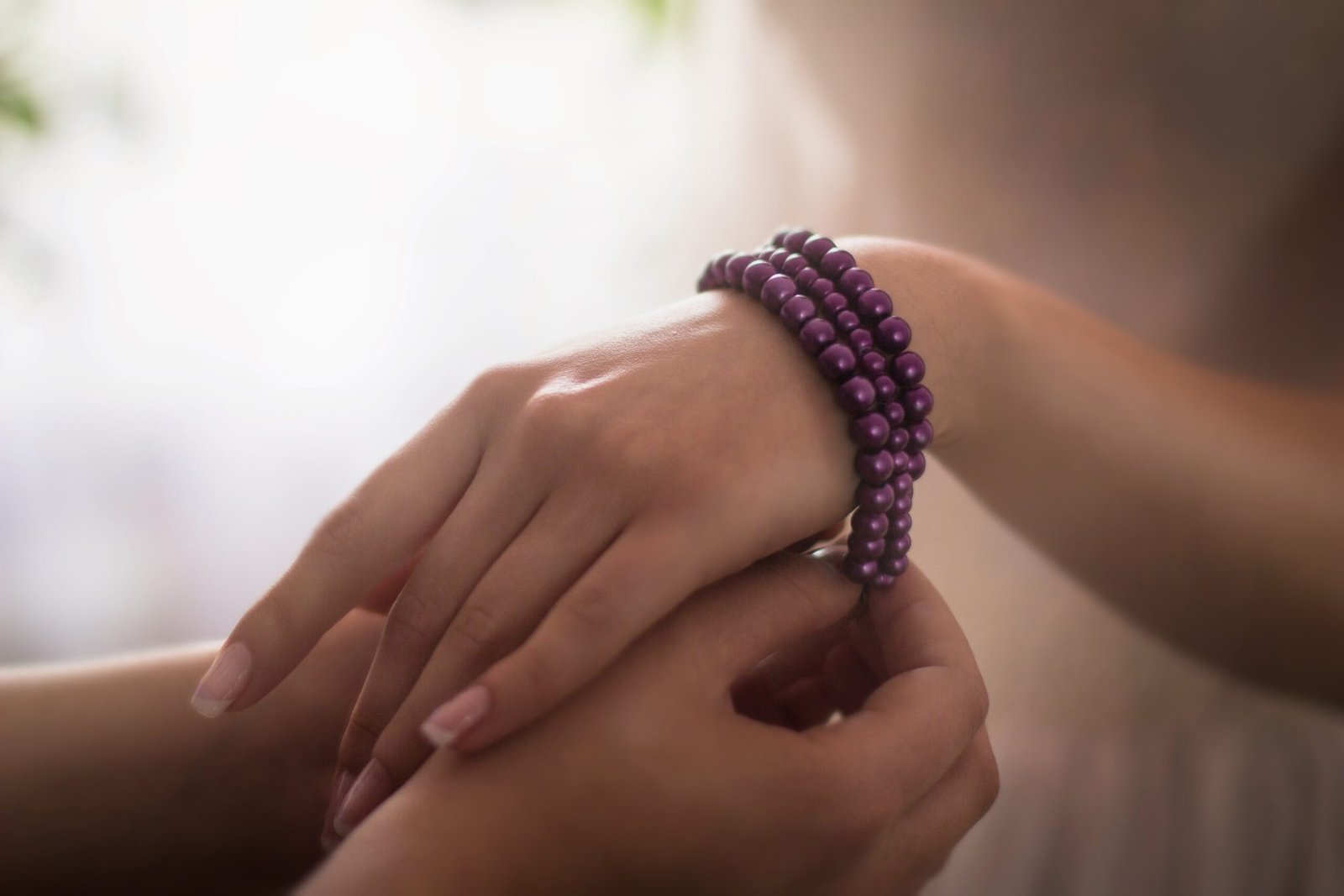 A closeup of a person putting a purple bracelet around the hand of a woman under the lights